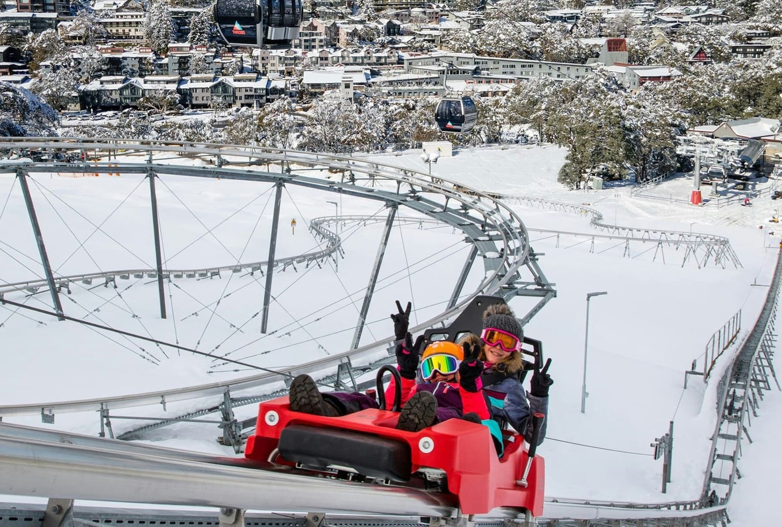 Two riders in a red cart on an elevated coaster track above the snow