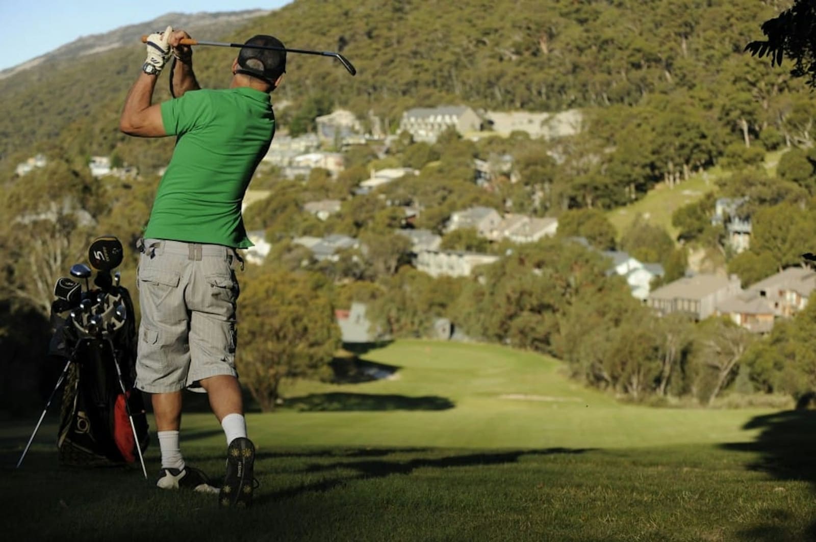 Golfer teeing off on a hillside fairway above the village