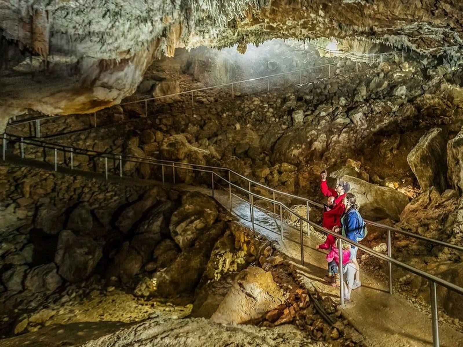 Visitors on a lit walkway through a limestone cave chamber